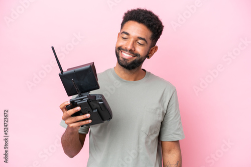 Brazilian man holding a drone remote control isolated on pink background with happy expression