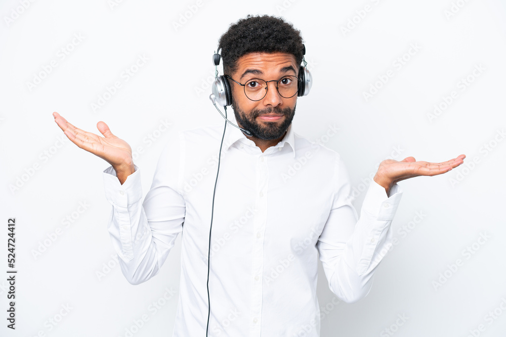 Telemarketer Brazilian man working with a headset isolated on white background having doubts while raising hands Telemarketer Brazilian man working with a headset isolated on white background having doubts while raising hands