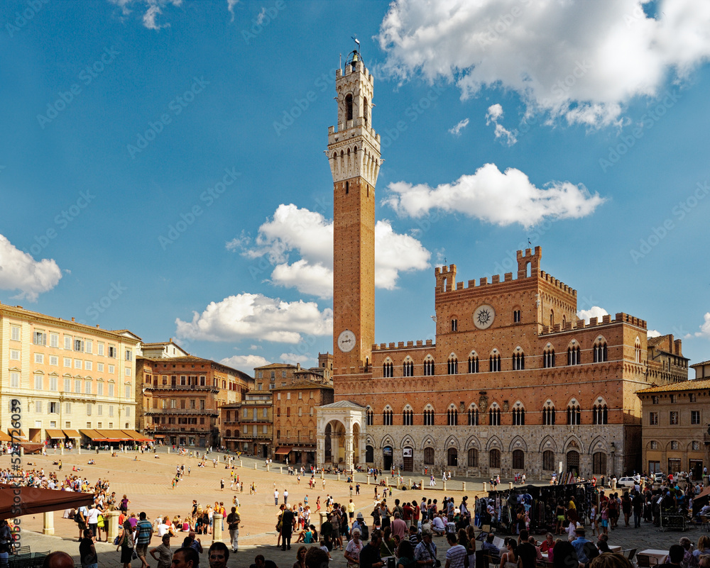 Tourists in the Piazza del Campo, the central square of the city of Sienna, Tuscany, Italy. Torre del Mangia tower rises behind