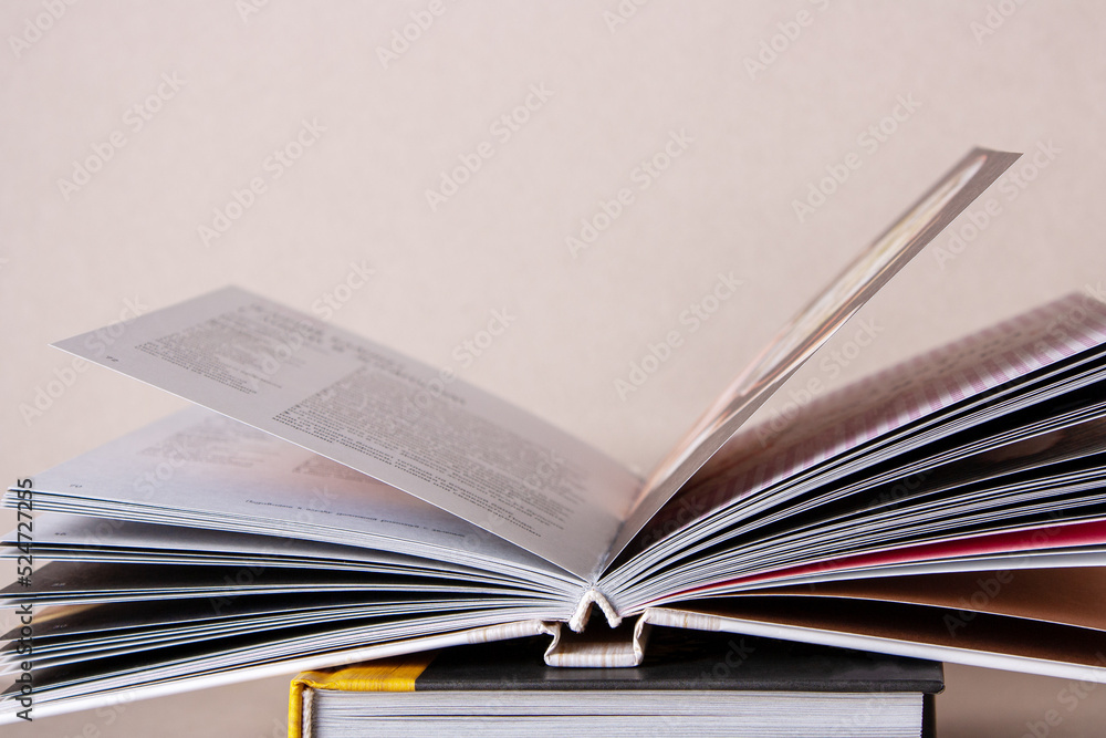 an open book lies on a stack of textbooks on a beige background, close-up an open book lies on a stack of textbooks on a beige background, close-up