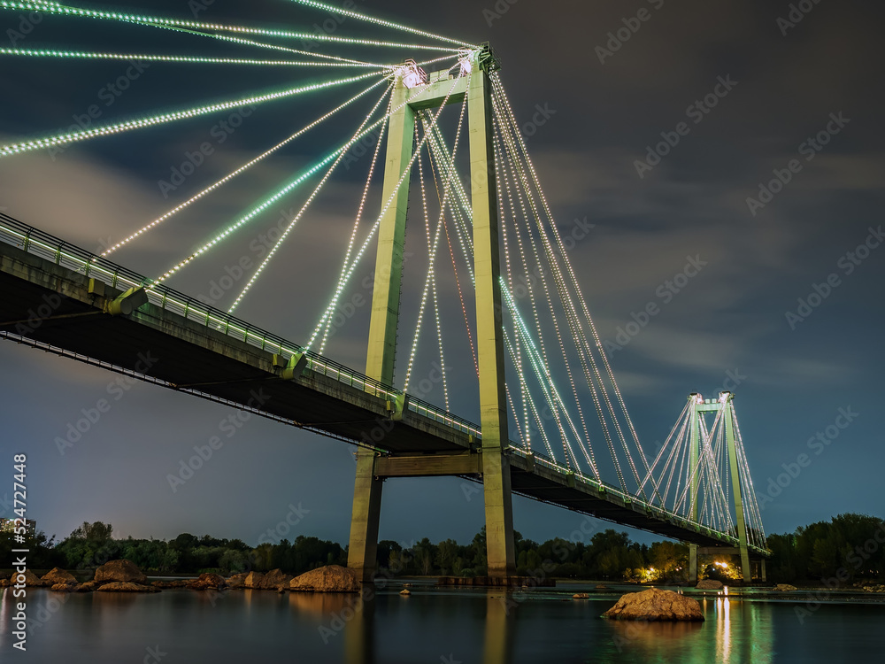 Naklejka premium Cable-stayed bridge across the river at night. Night illumination of buildings, reflections.