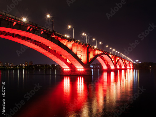 Arch bridge across the river at night. Night illumination of buildings, reflections.