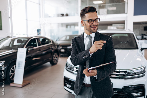 Wallpaper Mural Good looking, cheerful and friendly salesman poses in a car salon or showroom. Torontodigital.ca