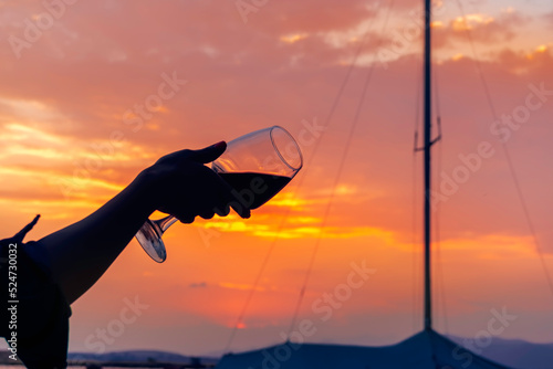 Silhouette of a female hand holding a glass of red wine in her hand on the seashore against the backdrop of a beautiful evening sunset