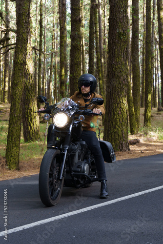 Motero con moto custom de ruta a través del bosque