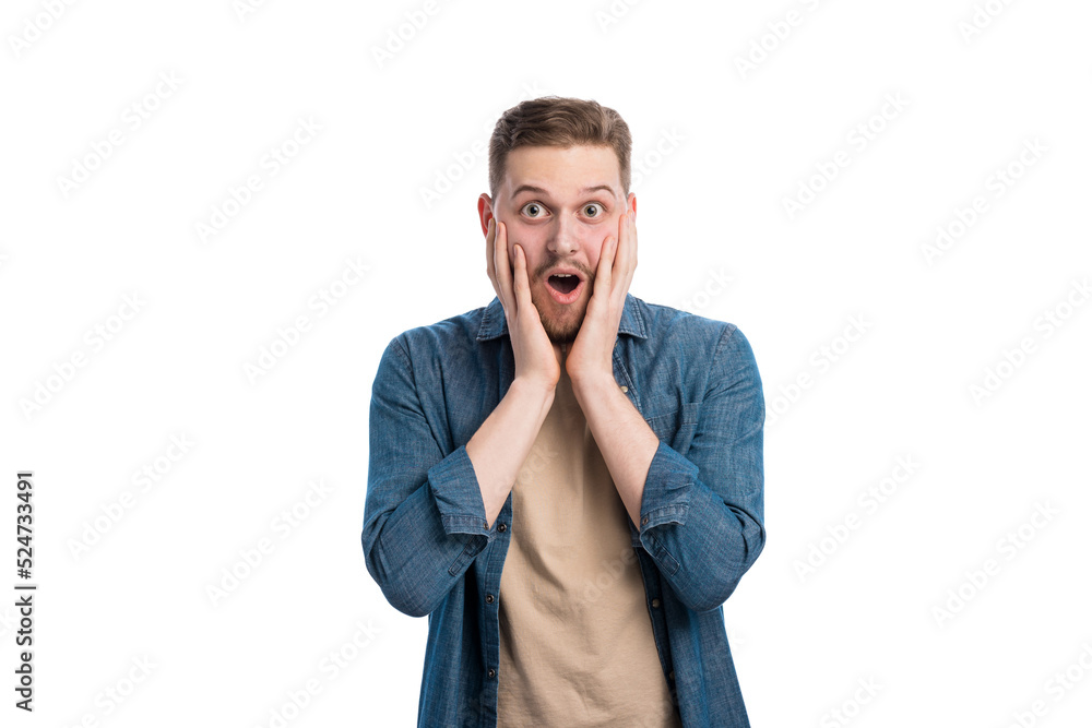 Caucasian young man with dropped jaw and wide opened eyes posing in bright studio. Shocked male person holding hands on cheeks and expressing surprisement.