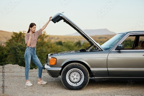 A woman stands outside a broken-down, dangerous old car with the hood open with a wrench on a road trip alone © SHOTPRIME STUDIO