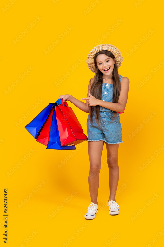 happy teen girl pointing finger on shopping bags on yellow background. full length
