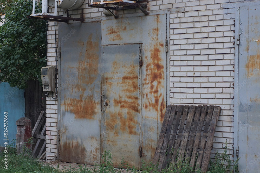 white brick facade of an old garage with a gray metal closed gate in brown rust on the street