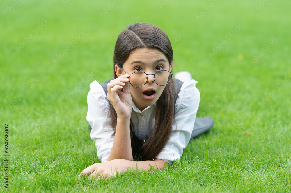 Portrait of surprised teen girl adjusting glasses lying on grass after school, surprise. Teen girl Portrait of surprised teen girl adjusting glasses lying on grass after school, surprise. Teen girl