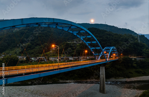 Empty blue bridge in mountain landscape with distant full moon at dusk