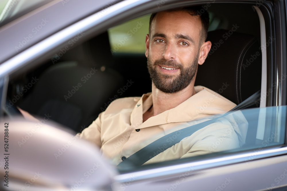 Portrait of confident smiling latin man driving a car looking at camera. Car sharing concept 