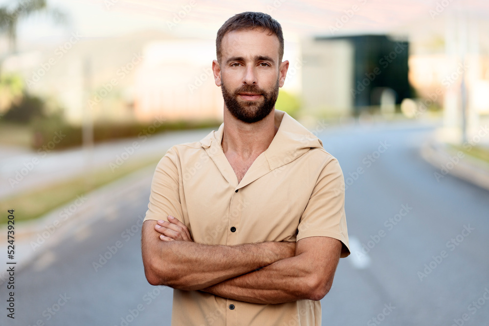Handsome stylish bearded man with arms crosses looking at camera standing on the street Handsome stylish bearded man with arms crosses looking at camera standing on the street