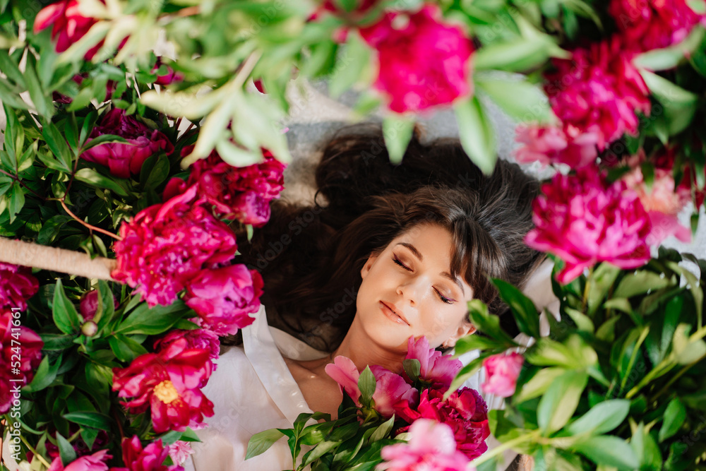 a beautiful and gentle young woman lies in peony flowers. feminine beauty. a beautiful and gentle young woman lies in peony flowers. feminine beauty.