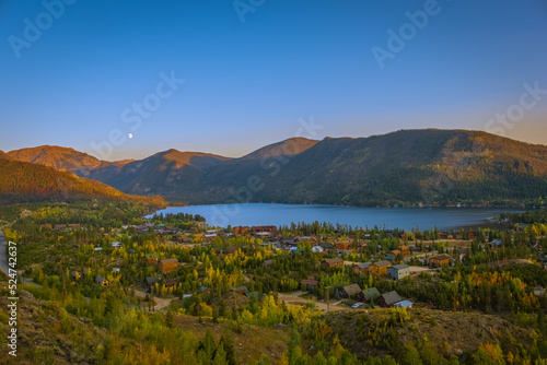 Beautiful view of mountain lake and town by the lake on nice fall evening in Colorado, USA. Blue sky, mountain range and rising moon in background