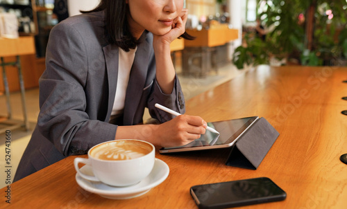 Busy young professional business woman using applications on digital tablet pad computer sitting at table in cafe remote working or learning online, writing holding stylus, close up view.