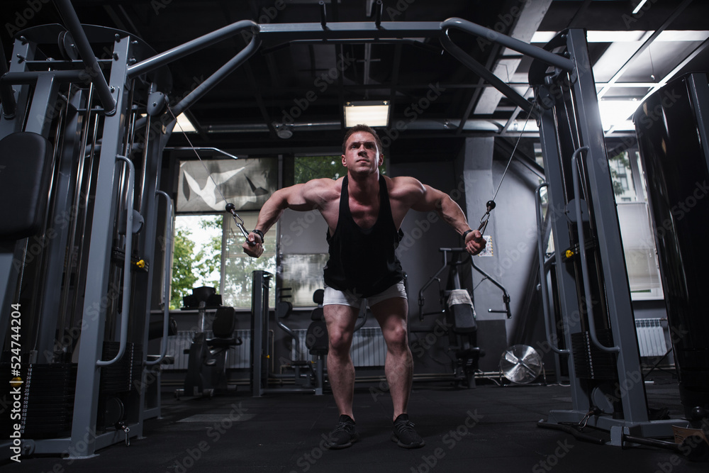 Full length shot of a bodybuilder exercising in cable crossover gym machine Full length shot of a bodybuilder exercising in cable crossover gym machine