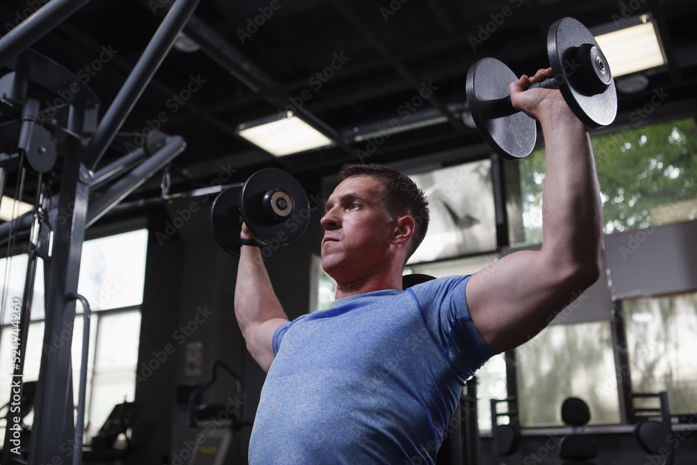 Low angle shot of a bodybuilder exercising with dumbbells at gym Low angle shot of a bodybuilder exercising with dumbbells at gym