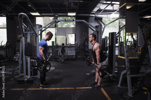 Twin brothers sportsmen facing each other at gym, doing barbell deadlift workout