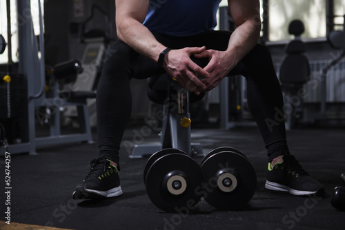Unrecognizable sportsman resting at the gym, dumbbells lying near on the floor