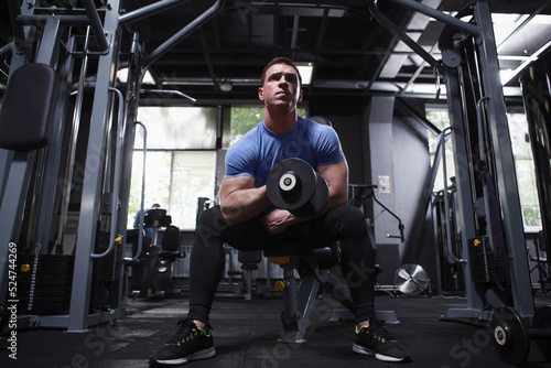 Full length shot of a muscular sportsman on weight training at gym, doing biceps curls with dumbbell