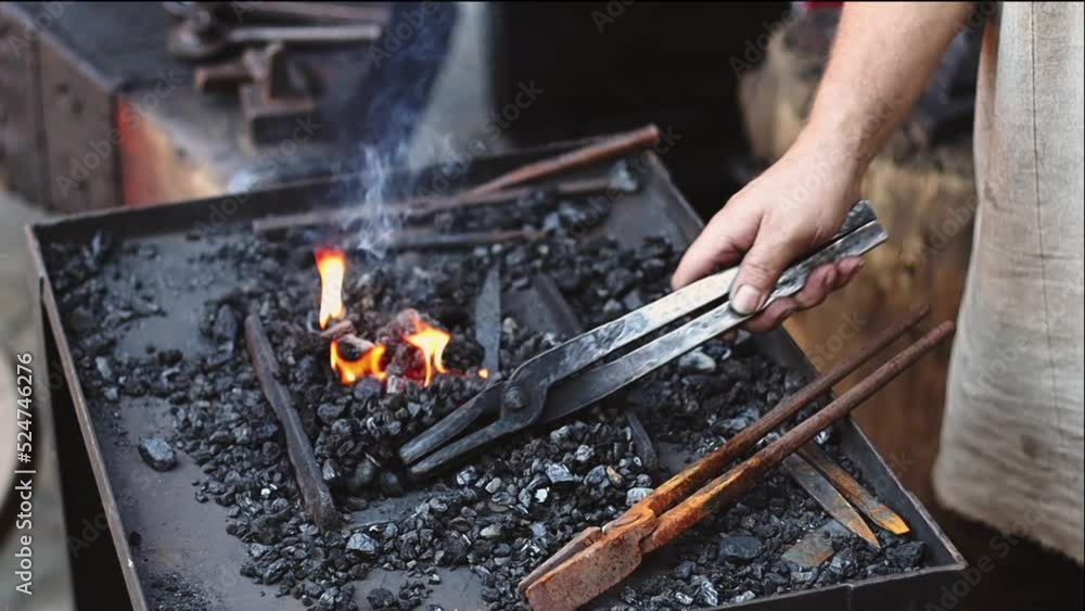 The hands of a caucasian male blacksmith of the middle ages close a red-hot knife with burning coals using tongs, close-up side view with slow motion and focus highlighting.Artisanal concept, medieval The hands of a caucasian male blacksmith of the middle ages close a red-hot knife with burning coals using tongs, close-up side view with slow motion and focus highlighting.Artisanal concept, medieval
