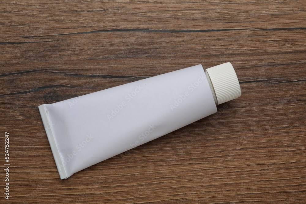 Fototapeta premium Blank white tube of ointment on wooden table, top view. Space for text