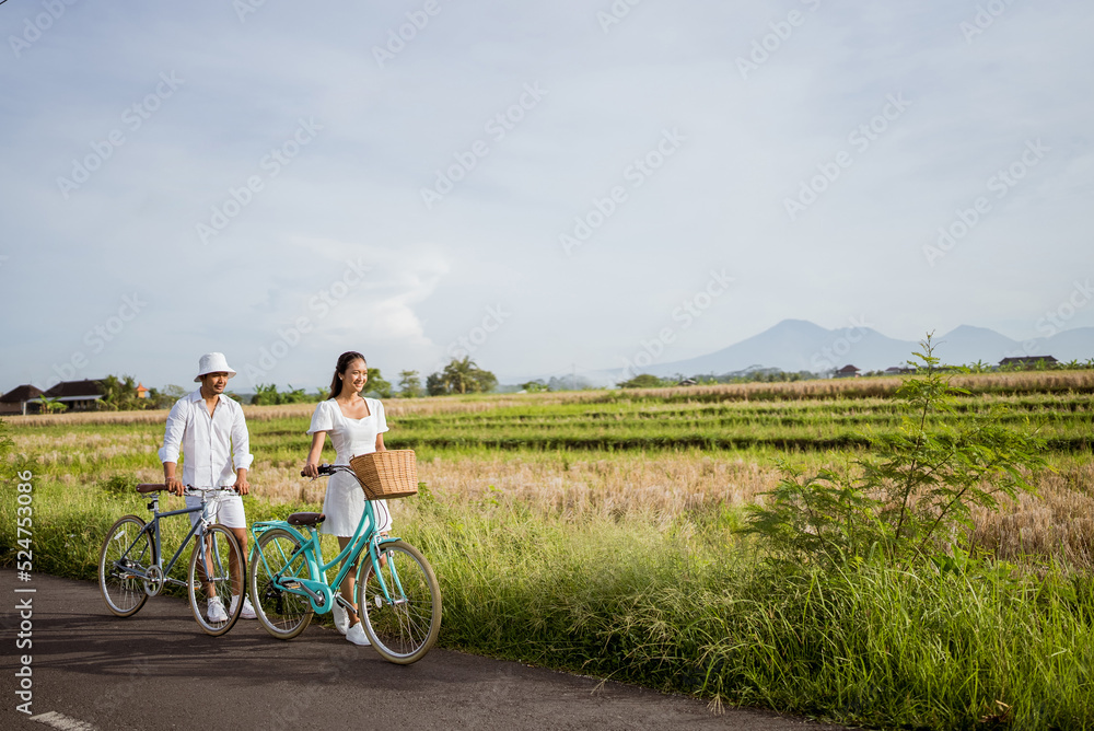 Obraz premium romantic couple push their bike as they are walking on the road in the countryside together