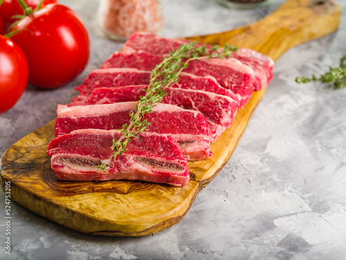 Close-up. Meat raw steaks with a sprig of rosemary on a cutting board, ripe red tomatoes, spices, seasonings on a gray background. Recipes for meat dishes.