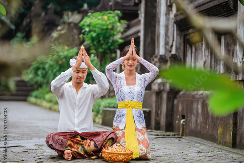 balinese couple do the prayer to god in the morning. hindu people make an offering to their god using canang photo