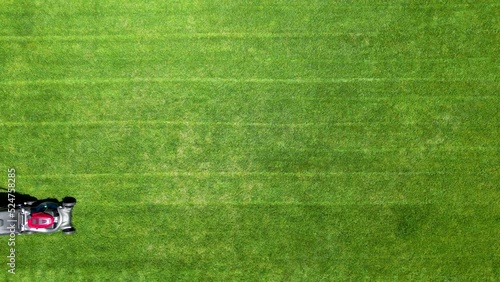 Aerial drone footage of an adult male homeowner mowing his backyard lawn on a sunny day.