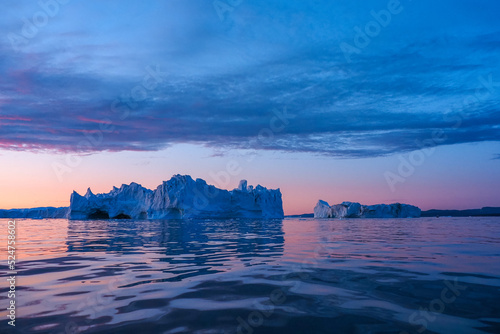 Majestic icebergs reflected in calm water under a vibrant pink and blue sunset sky in an Arctic landscape. photo