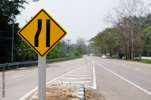 Yellow traffic square shaped left narrow lane sign at rural road Thailand to aware driver know Road narrows on left side ahead. Concept: Warning traffic sign for transportation. 