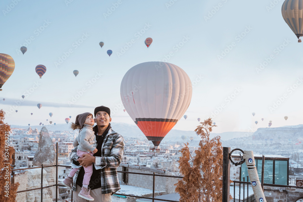 happy family looking at hot air balloon flying around them when visiting cappadocia turkey in winter - obrazy, fototapety, plakaty 