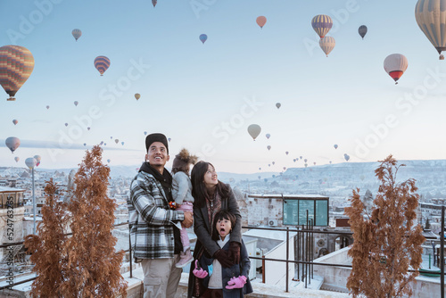 happy family looking at hot air balloon flying around them when visiting cappadocia turkey in winter photo