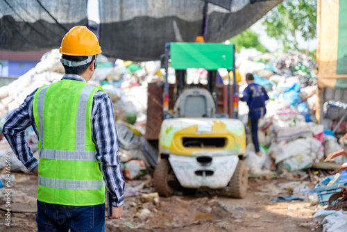 Male worker working at a recycling plant holding a tablet. Currently overseeing the disposal and recycling of waste at a small waste recycling plant.