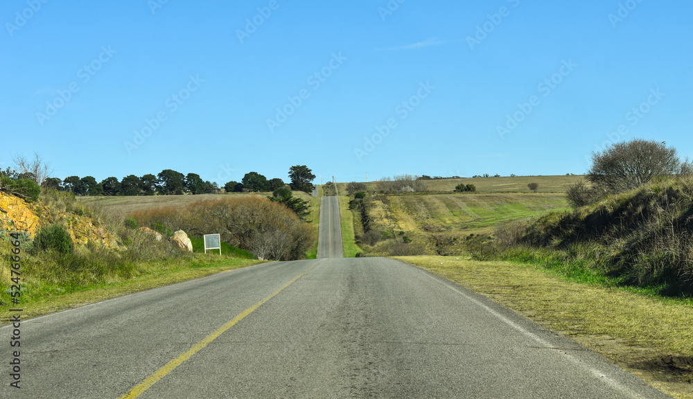 ruta en un camino montañoso, con cortes en la linea de vision por las subidas y bajadas, con cielo azul y paisaje verde