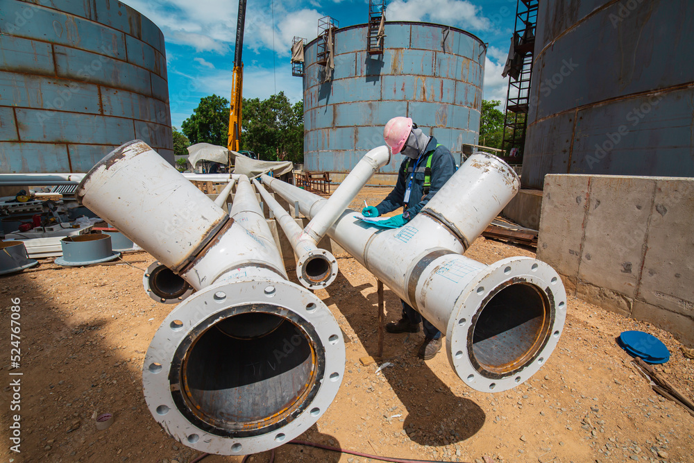 Male worker inspection at steel long pipes and pipe elbow new construction oil tank of visual check record pipeline oil and gas Male worker inspection at steel long pipes and pipe elbow new construction oil tank of visual check record pipeline oil and gas