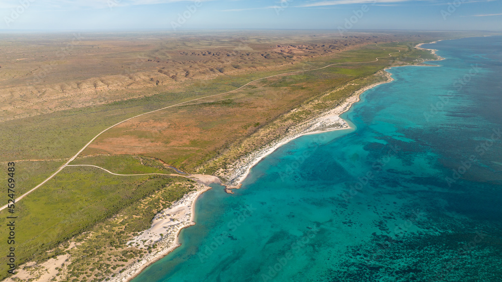 Areal view of the coastline in Cape Range National Park. The turquoise waters meeting the dry yet green bushland next to the rugged ridges of the range.