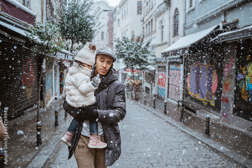portrait of father carrying his daughter during snow fall in the city