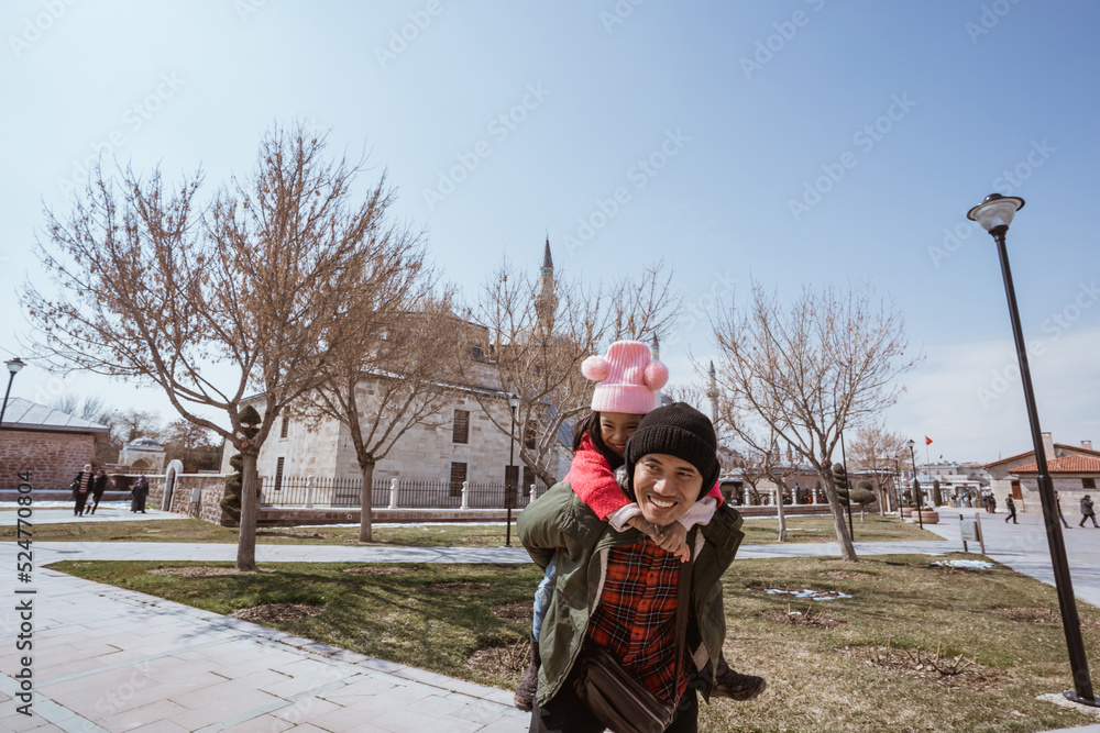 Obraz premium father carrying her daughter on his shoulder piggyback ride while visiting mosque in the city of konya turkey