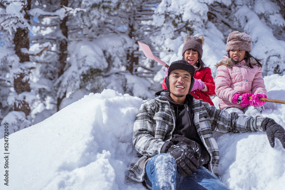 two girl and father smiling while sitting on a pile of snow enjoy their time in snowy winter together