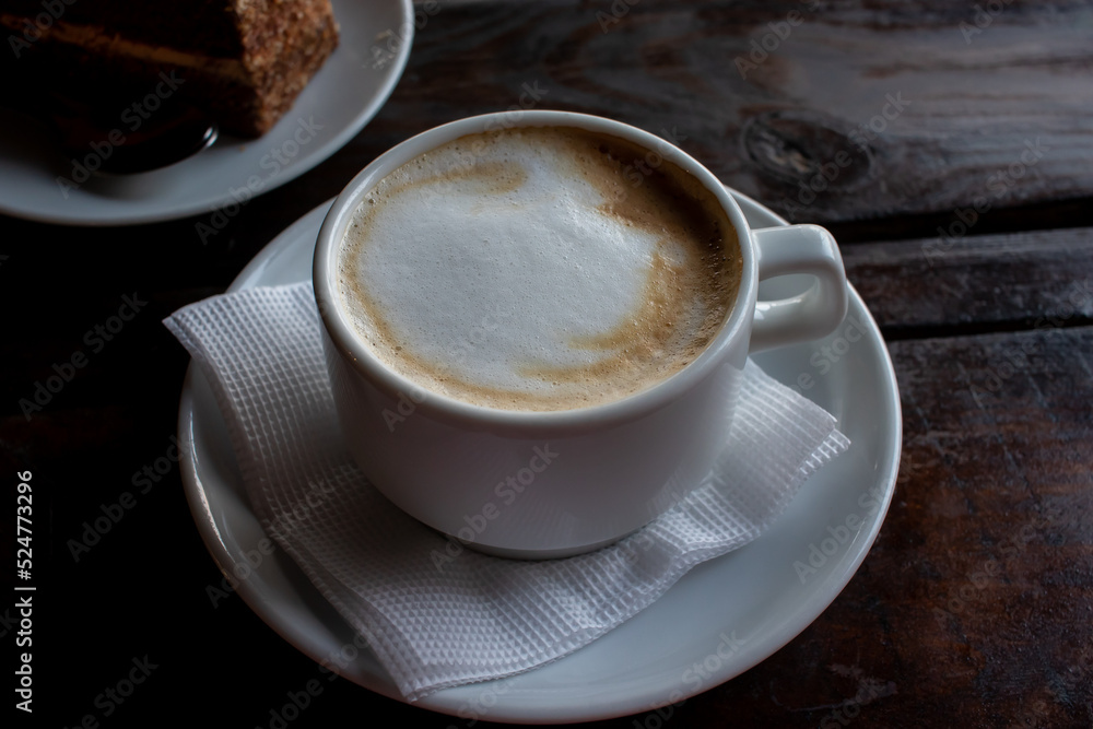 Cup of cappuccino and piece of cake on black wooden table. Cup of coffee with milk foam and dessert on dark background. Sunday morning coffee. Top view, flat lay