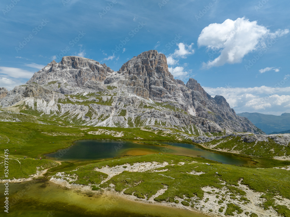 By the lake in the Italian Dolomites on a sunny summer day. People hiking in the hills. 