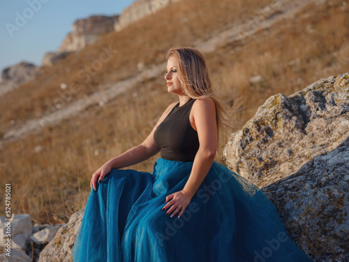Fashionable woman on desert field near mountain wearing black top and blue tulle skirt