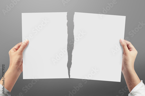 Hands tearing a sheet of white paper on gray background.