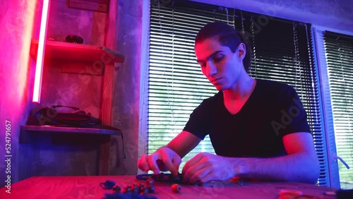 Craftsman makes dreamcatcher in dark workshop illuminated by neon light.