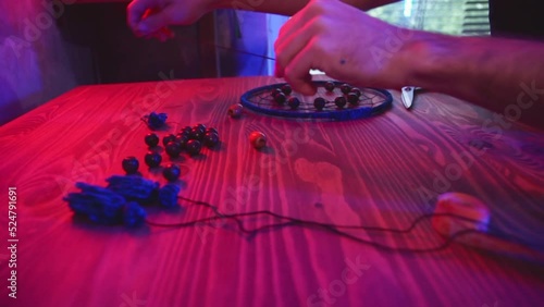Artisan makes dreamcatcher in art studio. Master in dark workshop with neon red and blue lighting.