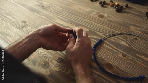 Artisan makes dream catcher in workshop. Craftsman works at wooden table, close up.