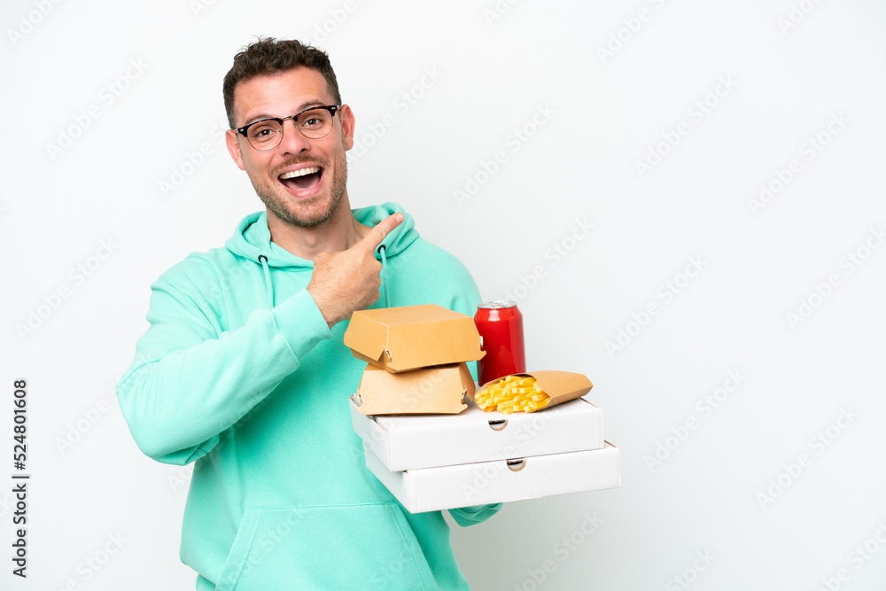 Young caucasian man holding fast food isolated on white background pointing back Young caucasian man holding fast food isolated on white background pointing back